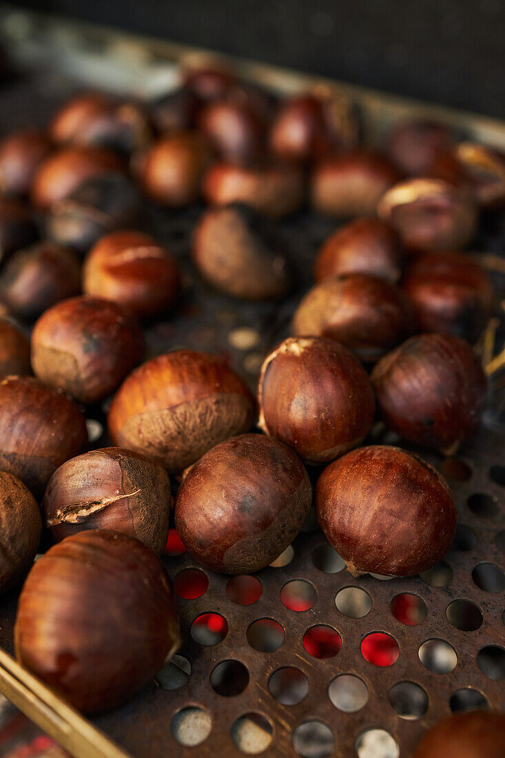 From above closeup of baked of pile of fresh chestnuts on metal tray near dry leaves on soil in autumn forest