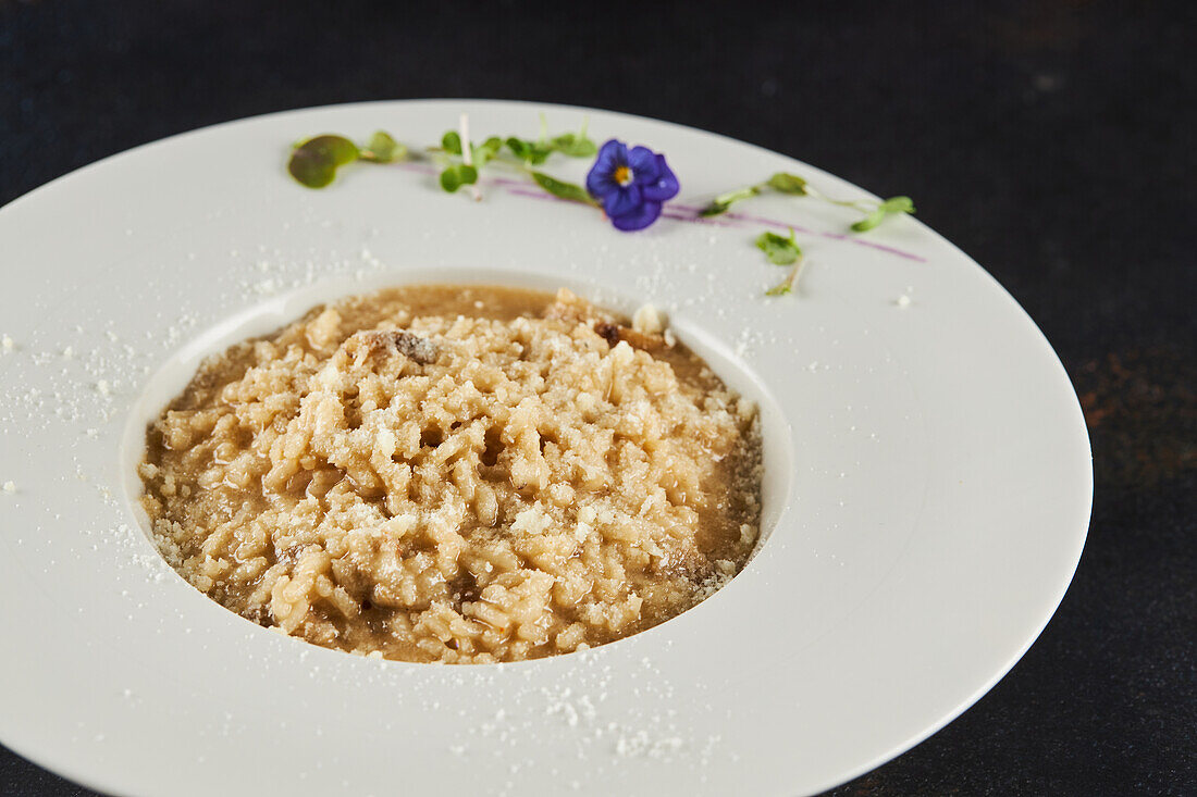 Delicious porchini mushroom risotto served on plate with sprouts and flower on dark background