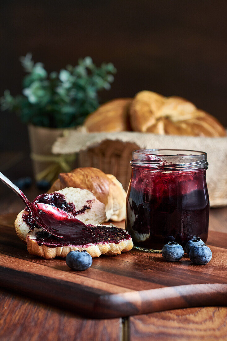 Vorbereitung eines Frühstücks mit Croissants und Blaubeermarmelade auf einem Holztisch