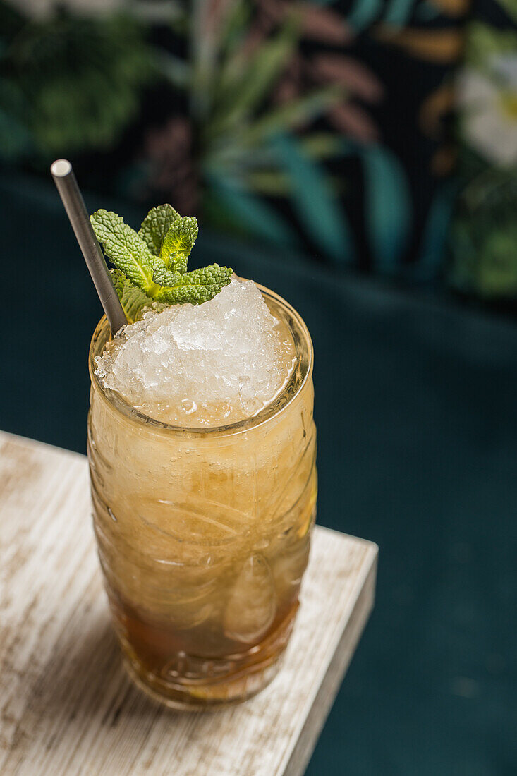 From above of tiki cup with cold alcohol drink with straw served with ice and decorated with fresh herb placed on blurred background