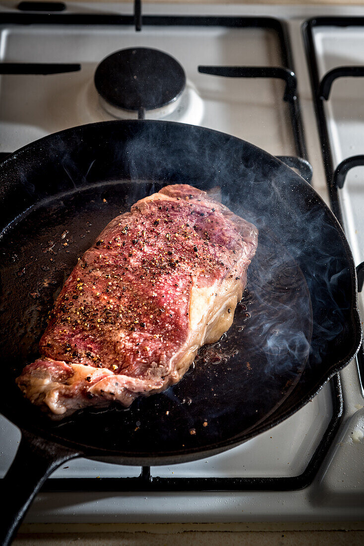 From above of pan with appetizing meat piece with condiments and in melted butter on gas stove