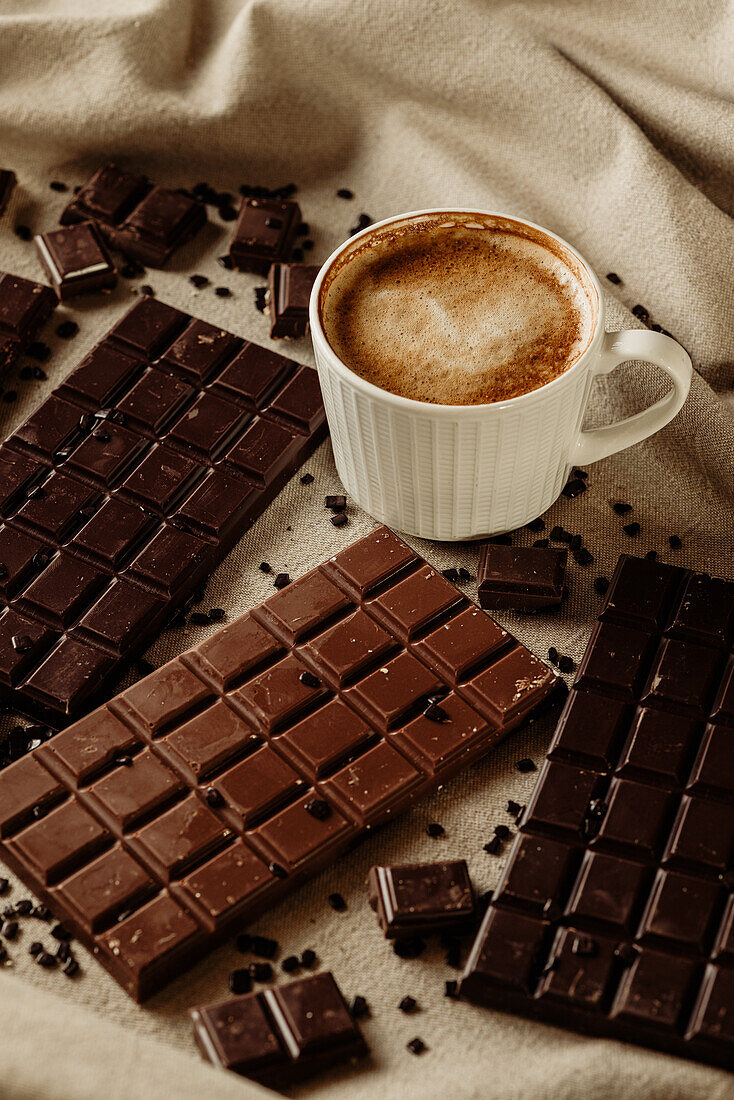 From above cup of hot aromatic coffee placed on wooden table near piece of chocolate bars with