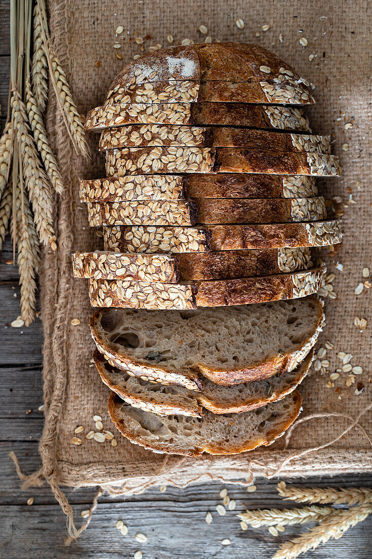 Overhead row of sourdough bread pieces with seeds on crust placed on sackcloth near wheat ears and scattered grains