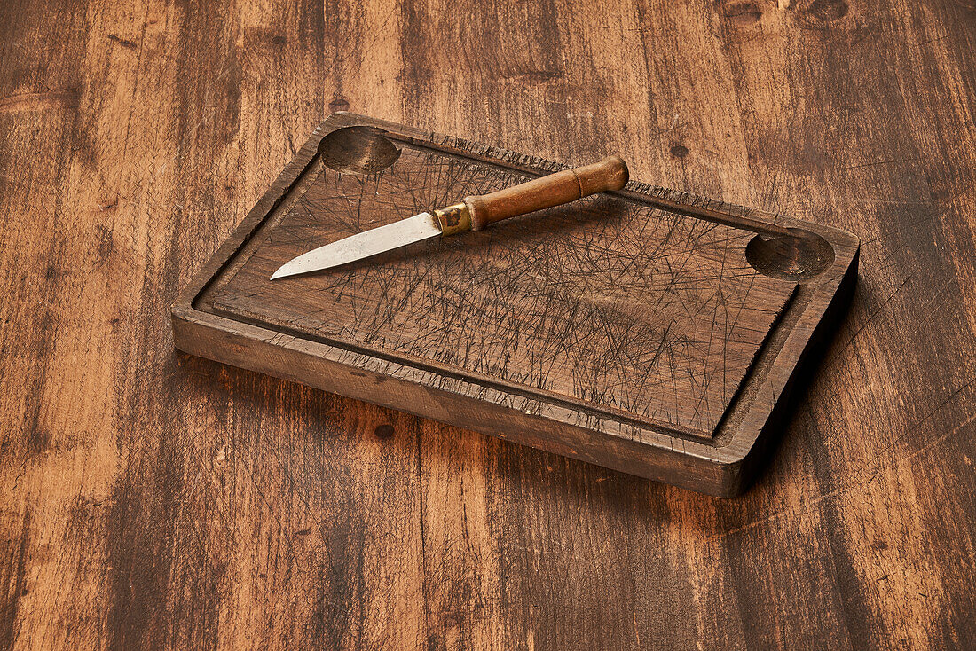 From above scratched chopping board with sharp knife placed on rustic lumber table