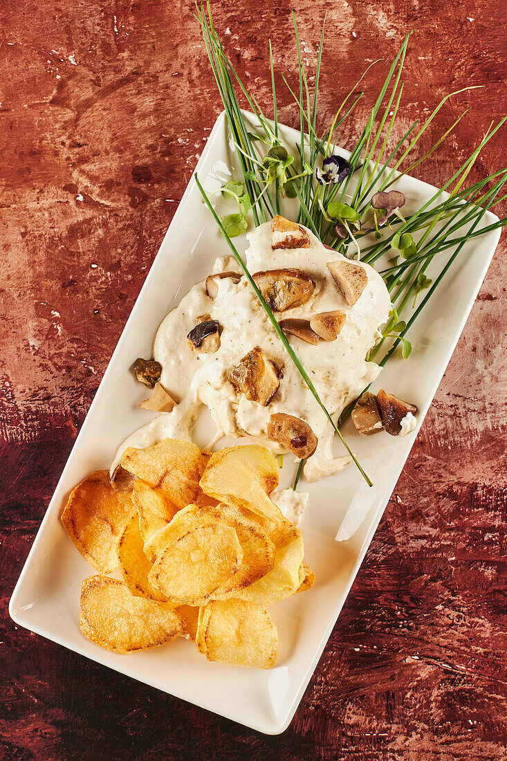 Draufsicht auf köstliche Fleischmedaillons und Bratkartoffeln mit Käsesauce und Grünzeug auf braunem Tisch in Restaurant
