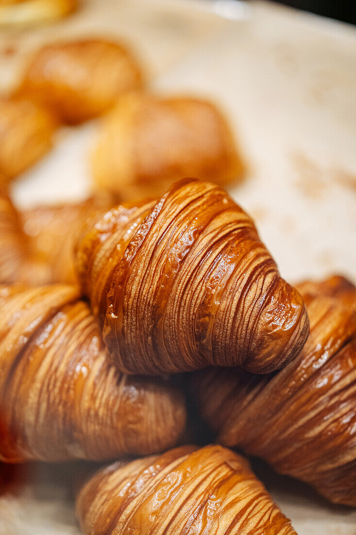 Heap of tasty crispy brown croissants placed on parchment in showcase of modern light confectionery with pastry on blurred background