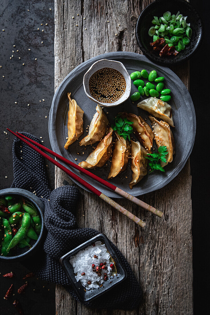 Gyozas mit grünen Bohnen und Sojasauce mit Sesam werden mit Stäbchen neben Schalen mit Gewürzen und Erbsenschoten platziert