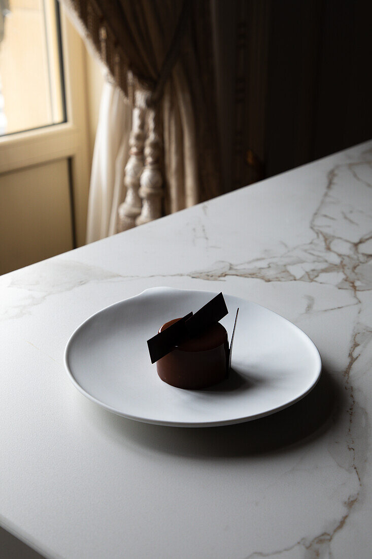 Blick von oben auf einen leckeren Schokoladenkuchen mit essbarer Dekoration auf einem weißen Teller und auf einem Marmortisch