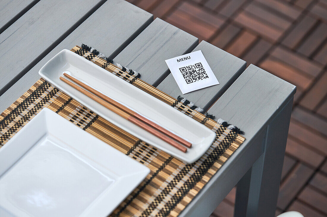 Blick von oben auf ein Stück Papier mit QR-Code der Speisekarte, die auf einem Tisch mit Stäbchen und Teller in einem asiatischen Restaurant liegt