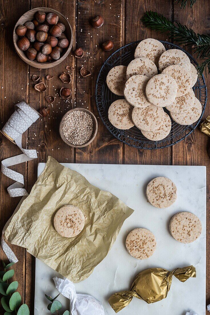 Draufsicht auf eine Reihe süßer, runder Butterkekse mit Haselnüssen, die mit Geschenkpapier und Bändern auf einem Holztisch arrangiert sind