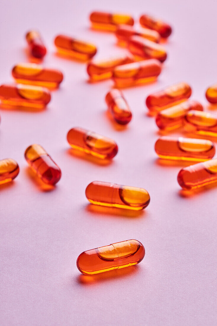 Composition of orange pills scattered on pink background in light studio
