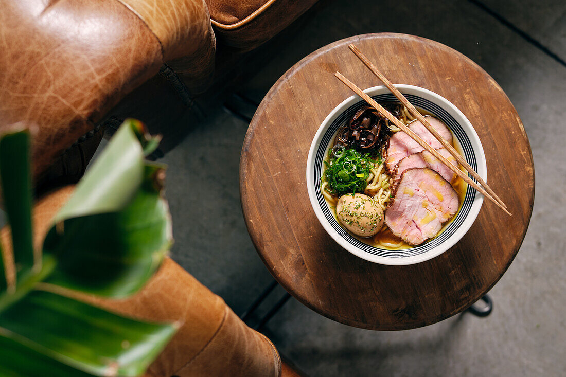 Draufsicht auf eine köstliche traditionelle Ramen-Suppe in einer Schale mit Stäbchen, serviert auf einem runden Tisch