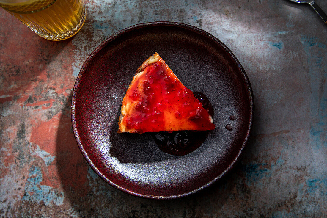 From above of appetizing pie wit berry jam placed on ceramic plate with glass of drink with ice in restaurant