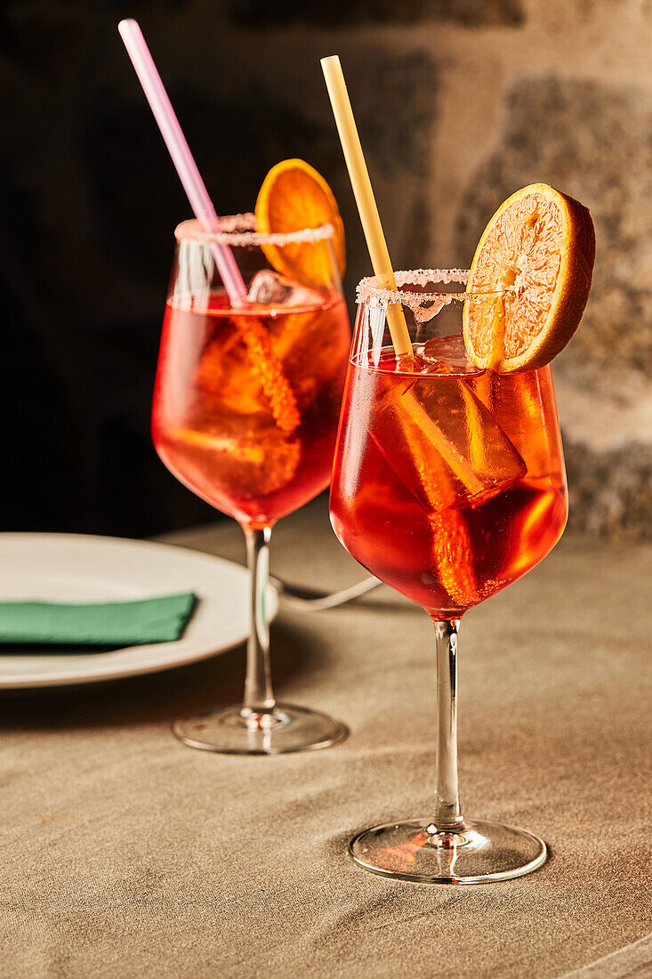 Aperol Spritz cocktail garnished with sugar and blood orange slices in glass goblets with straws on table in restaurant