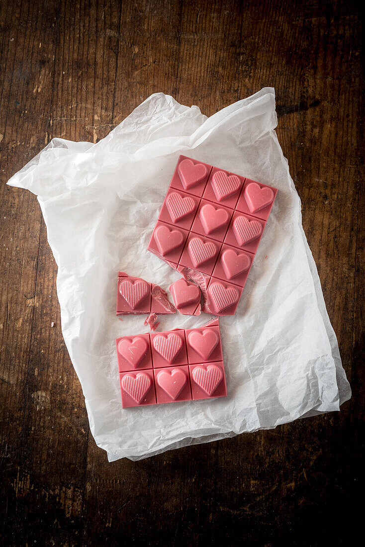 Top view minimalistic composition with pieces of handmade pink chocolate bar with heart shaped design on wooden background