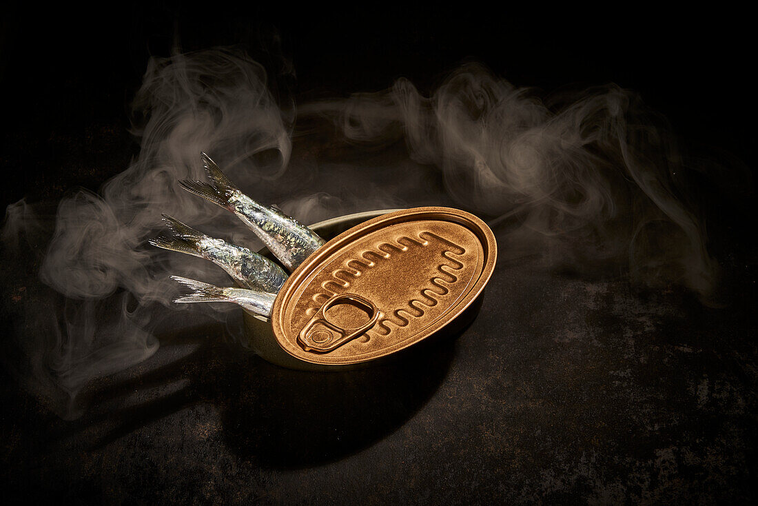 From above of canned fish in tin can with opened placed on black background with smoke in room with dim light