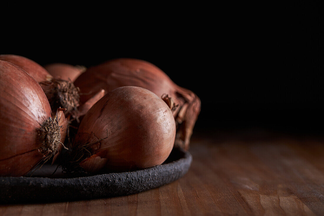 Bunch of fresh unpeeled onions placed on plate on timber table