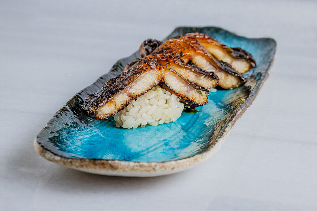 Grilled smoked eel nigiri over blue ceramic plate