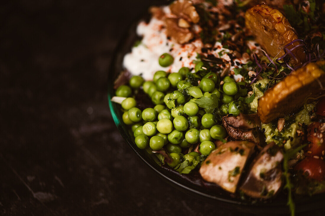 Bowl of tasty sweet potato slices with cherry tomatoes near green peas and sesame seeds on dark background