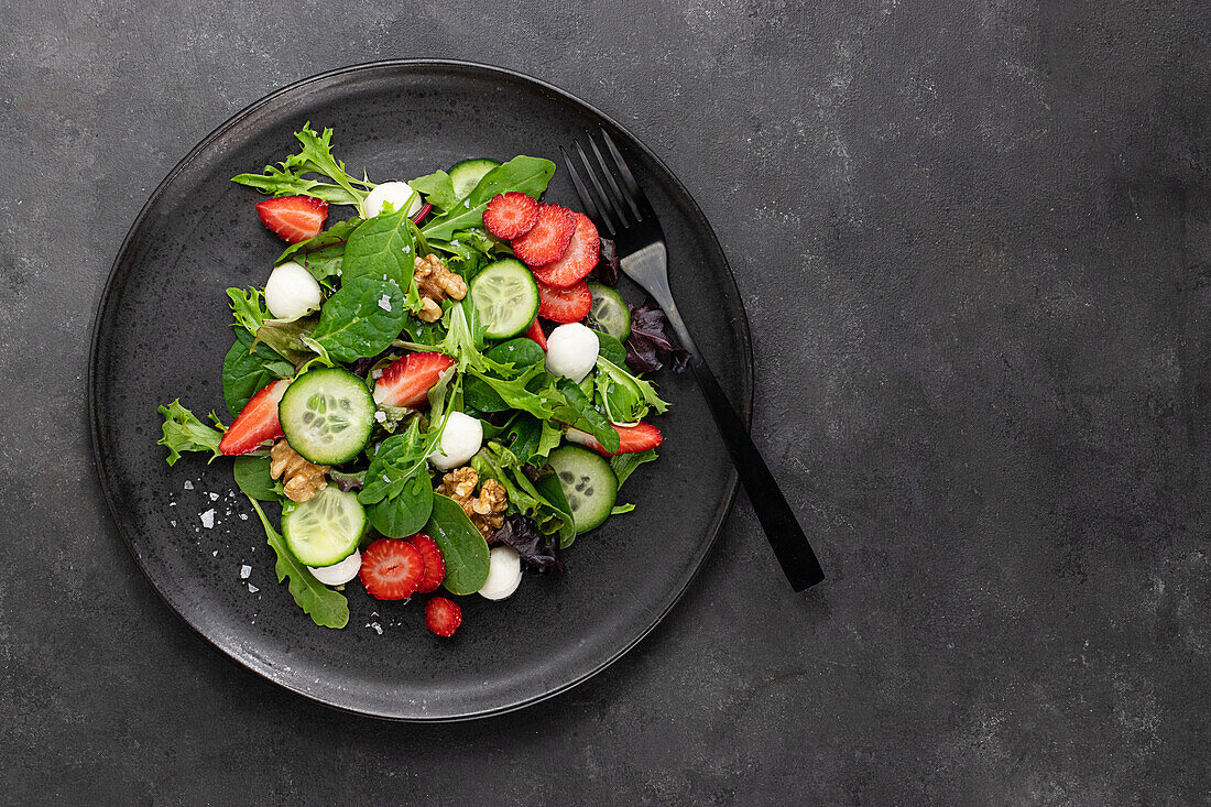 Teller mit einem Sommersalat aus Erdbeeren und Gurken auf einem dunklen Tisch