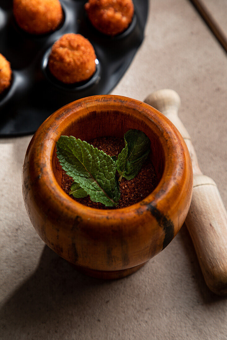 From above of wooden mortar with pepper powder and mint leaves near pestle placed near deep fried cheese balls