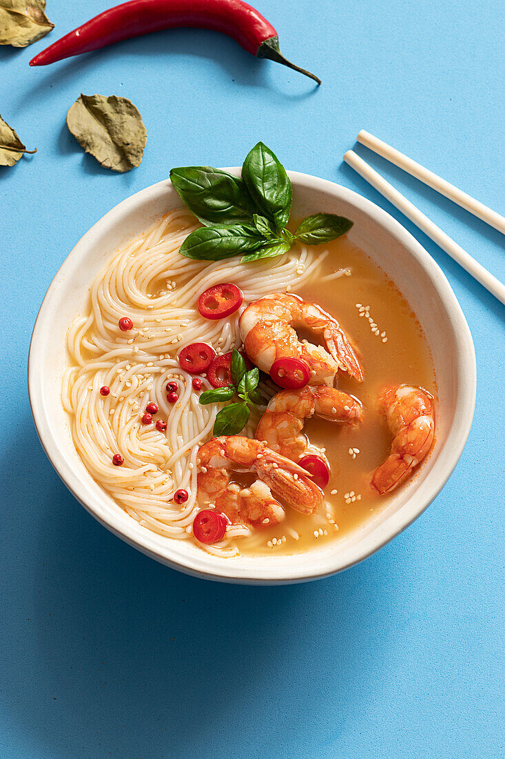 Tom-Yum-Suppe in Schüssel mit Stäbchen auf blauem Hintergrund