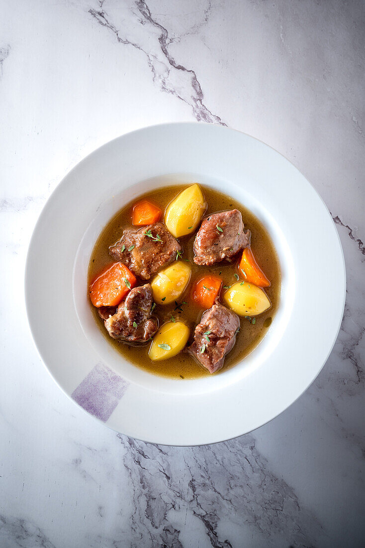 From above of appetizing stew with vegetables and meat served in plate on marble table