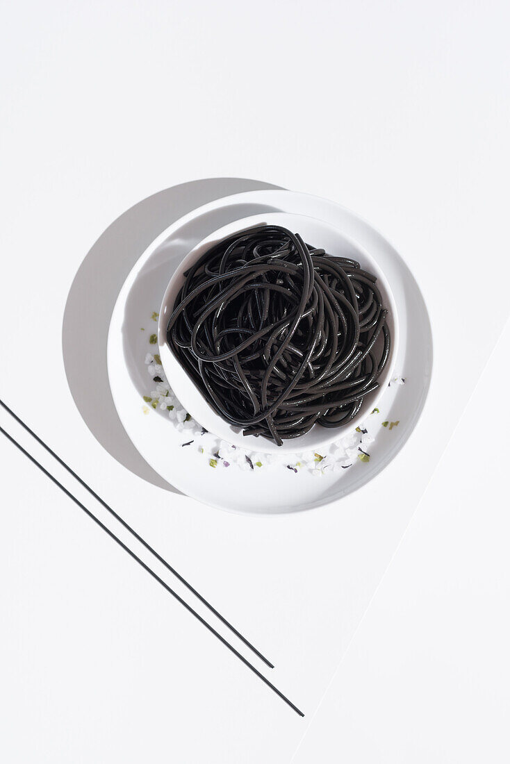 From above of ceramic bowl with delicious spaghetti with black squid ink with chopsticks on white background