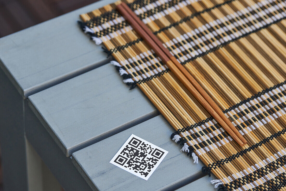 Hochformatiger QR-Code der Speisekarte eines asiatischen Restaurants auf einem Tisch mit Serviette und Stäbchen