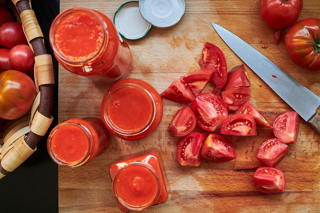 Draufsicht auf reife rote Tomaten und Gläser mit Soße auf einem Tisch in der Küche