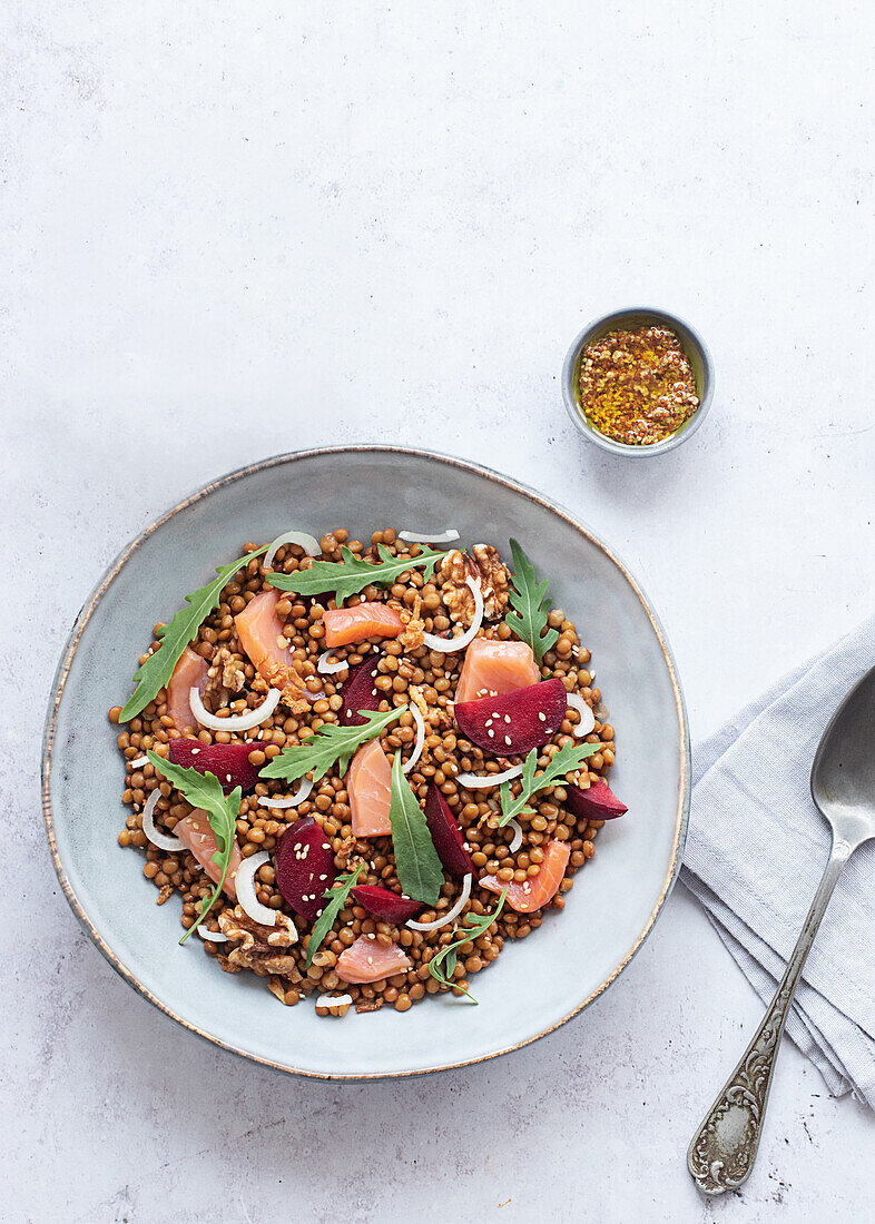 Nahaufnahme eines Lachs- und Linsensalats von oben auf einem Tisch mit rosa Tischtuch