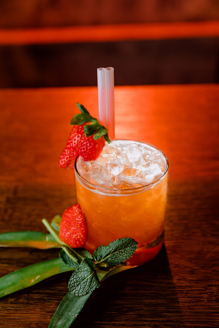 Blick von oben auf einen San-Francisco-Cocktail aus Wodka und Orangensaft, garniert mit Erdbeeren und Eiswürfeln auf Palmenblättern