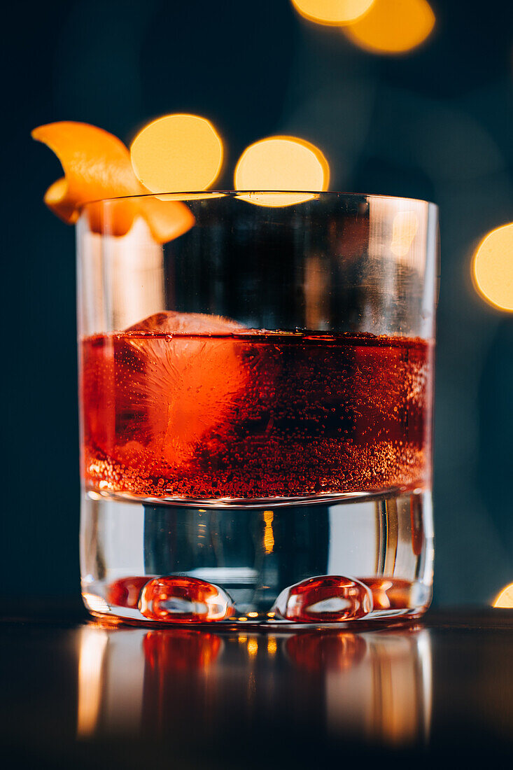 Glass of refreshing alcoholic Negroni cocktail garnished with ripe orange peel and placed on table amidst barman tools