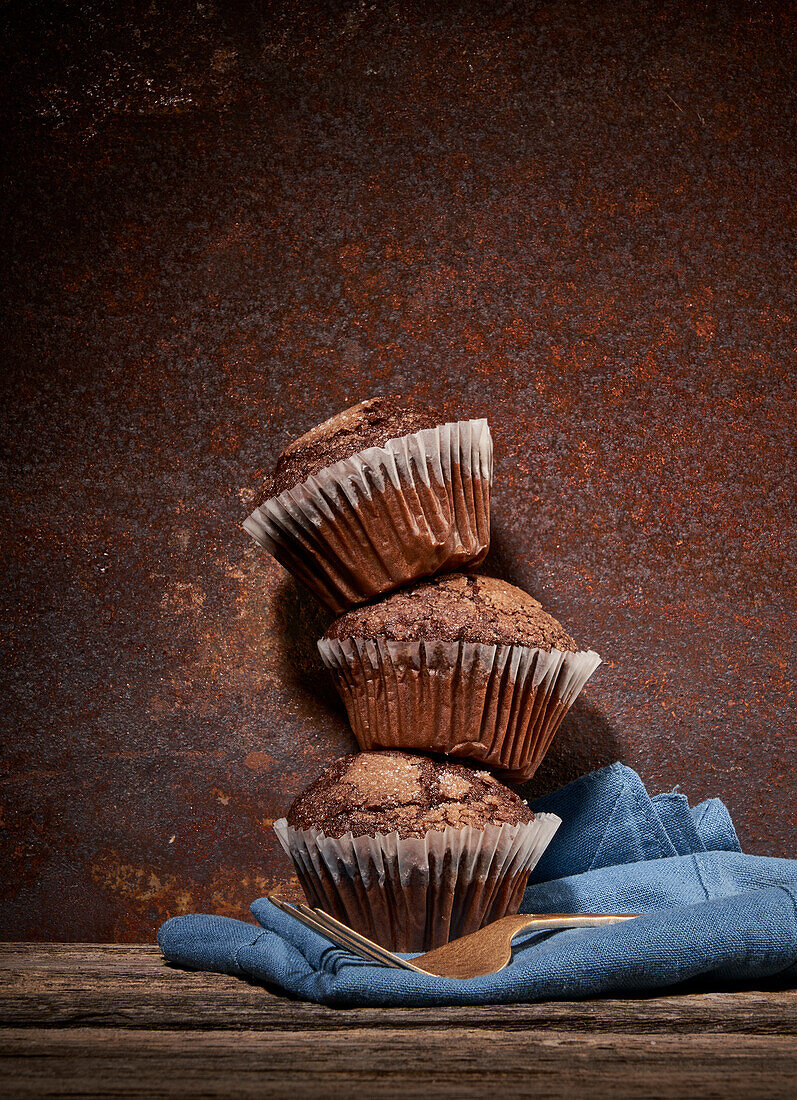 Stapel leckerer süßer Schokoladenmuffins übereinander auf einem Holztisch mit blauem Handtuch und Gabeln
