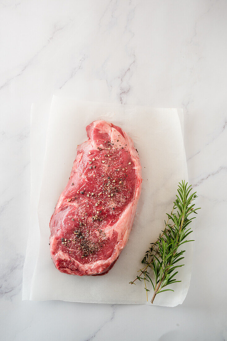 Overhead view of uncooked meat piece with thyme leaves against baking paper on marble background