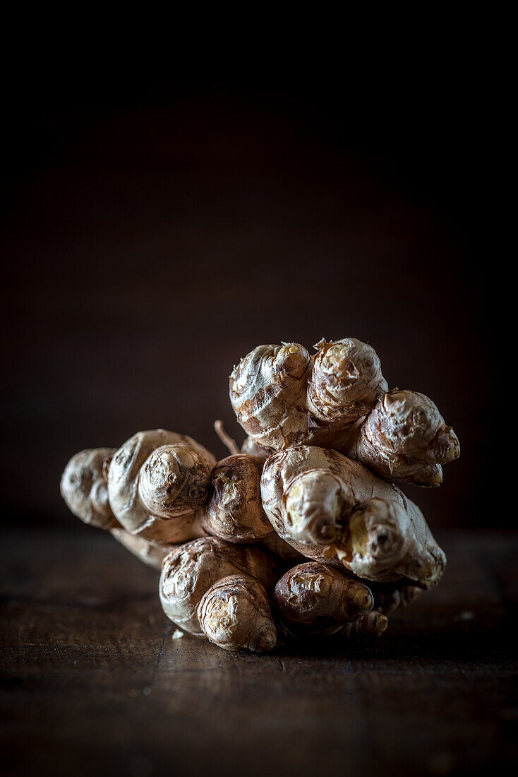 Still life composition with tubers of Jerusalem artichoke also called sunroot or topinambur olaced on wooden table against black background