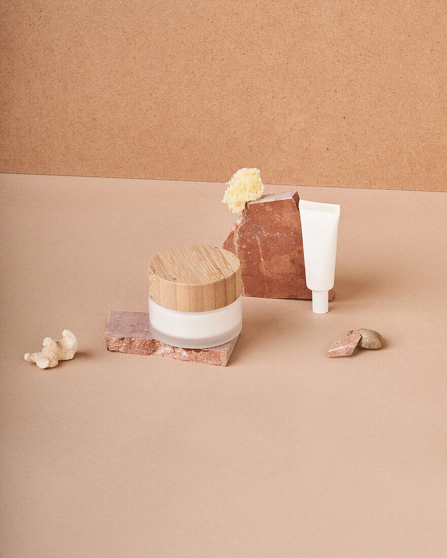 Jar and tube of cream with handmade organic soap pieces near pumice stone on two color background