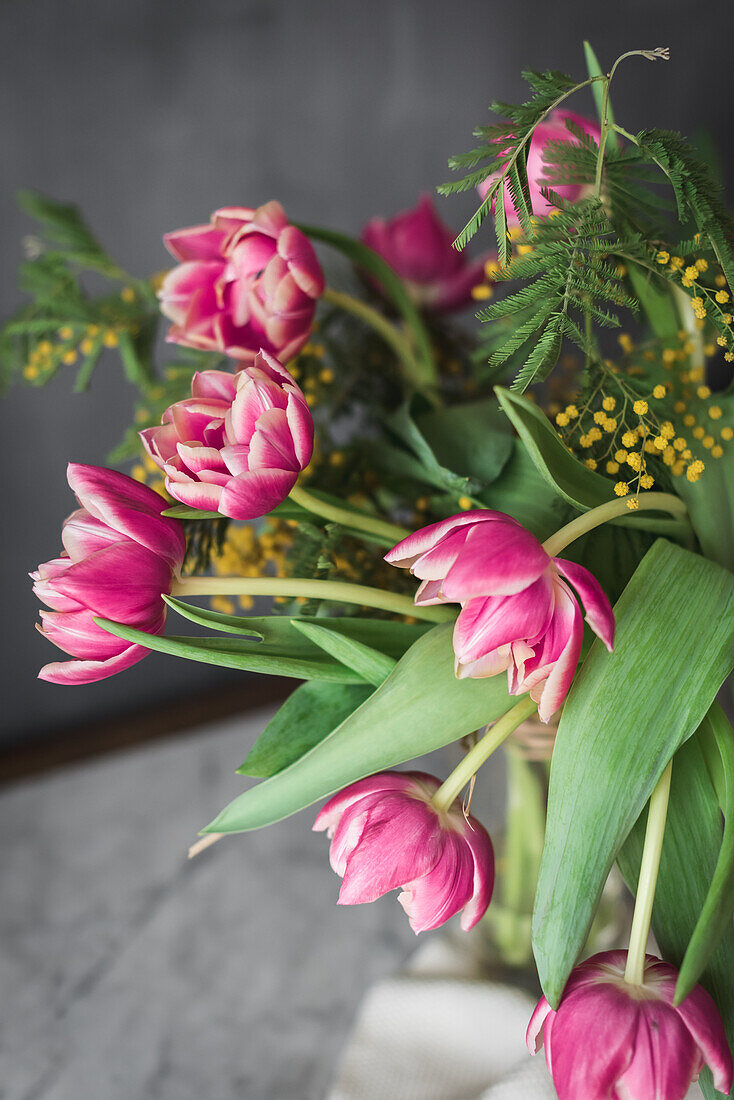 Blühende rosa Blumen mit zarten Blütenblättern und grünen Blättern in einer Vase auf grauem Hintergrund