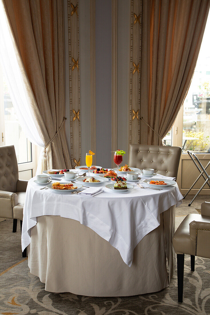 Various colorful dishes and juices served on round table during breakfast in elegant hotel restaurant in sunny morning