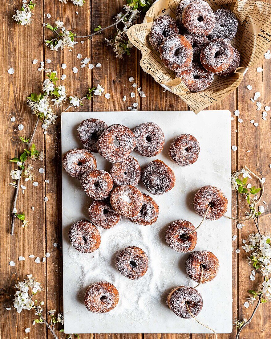 Draufsicht auf appetitanregende geliehene Donuts, die auf einer weißen Tafel auf einem Holztisch mit Blumen angeordnet sind