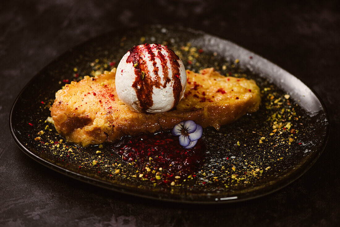 Leckerer French Toast mit Baiser-Milch-Eiskugel, bedeckt mit süßer Beerensauce auf einem Teller mit Gewürzen im Restaurant auf dunklem Hintergrund