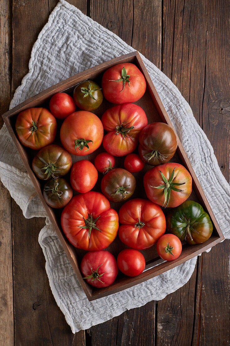 Draufsicht auf frische reife rote Tomaten in einer Holzkiste auf einer Leinenserviette auf dem Tisch