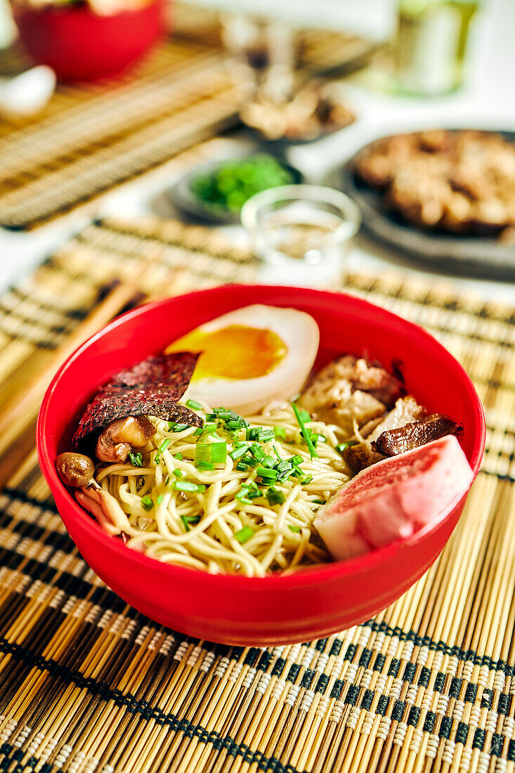 Von oben auf appetitliche Ramen-Suppe mit Fleisch und Ei und Nudeln, serviert in einer Schüssel auf einem Tisch neben Stäbchen und einer Glastasse