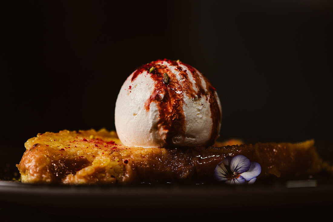 Low angle view of yummy French toast with meringue milk ice cream scoop covered with sweet berry sauce on plate with condiments in restaurant on dark background