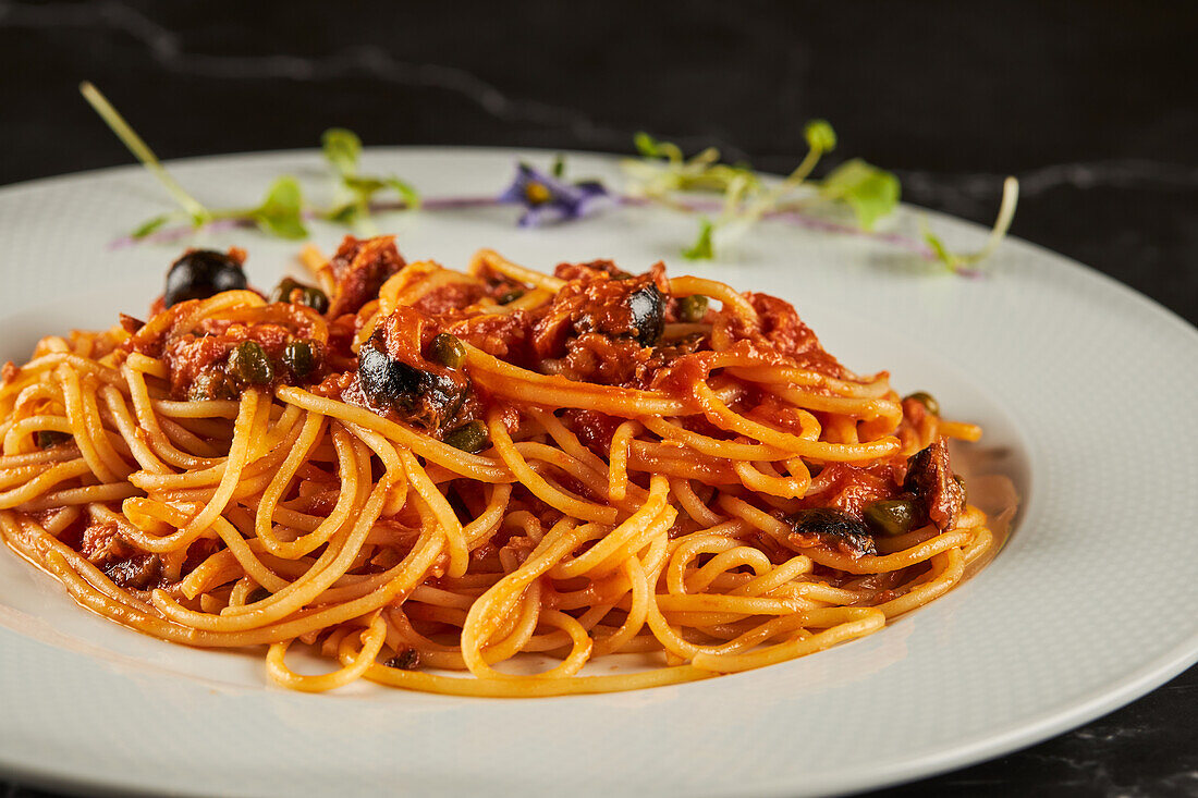 Nahaufnahme von leckeren Spaghetti alla puttanesca mit Tomatensoße und Meeresfrüchten, garniert mit Knoblauch und Chilischoten, serviert auf einem Teller in einem italienischen Restaurant