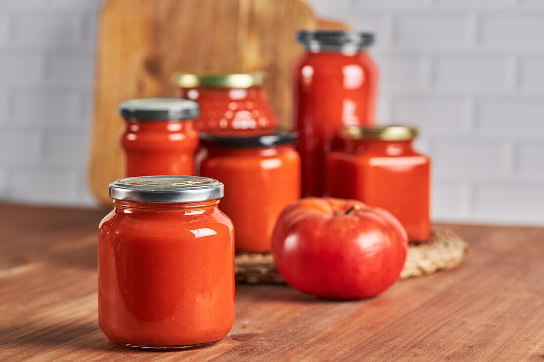 Sealed glass jar with handmade tomato sauce placed on table in kitchen at home