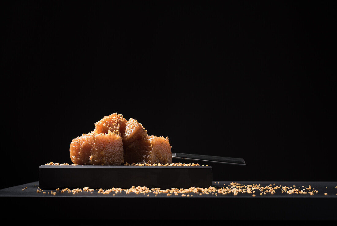 Gourmet quince jelly paste in ceramic plate sprinkled with sesame seeds on black background