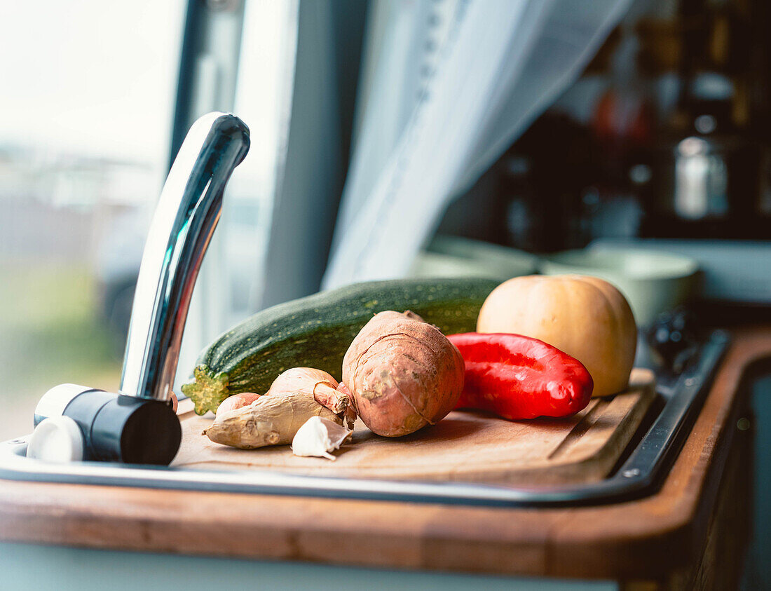 Rohes Gemüse, darunter Zucchini, Kürbis, Paprika und Süßkartoffeln, auf einem Schneidebrett für die Zubereitung in einem Wohnwagen während einer Reise in Kantabrien