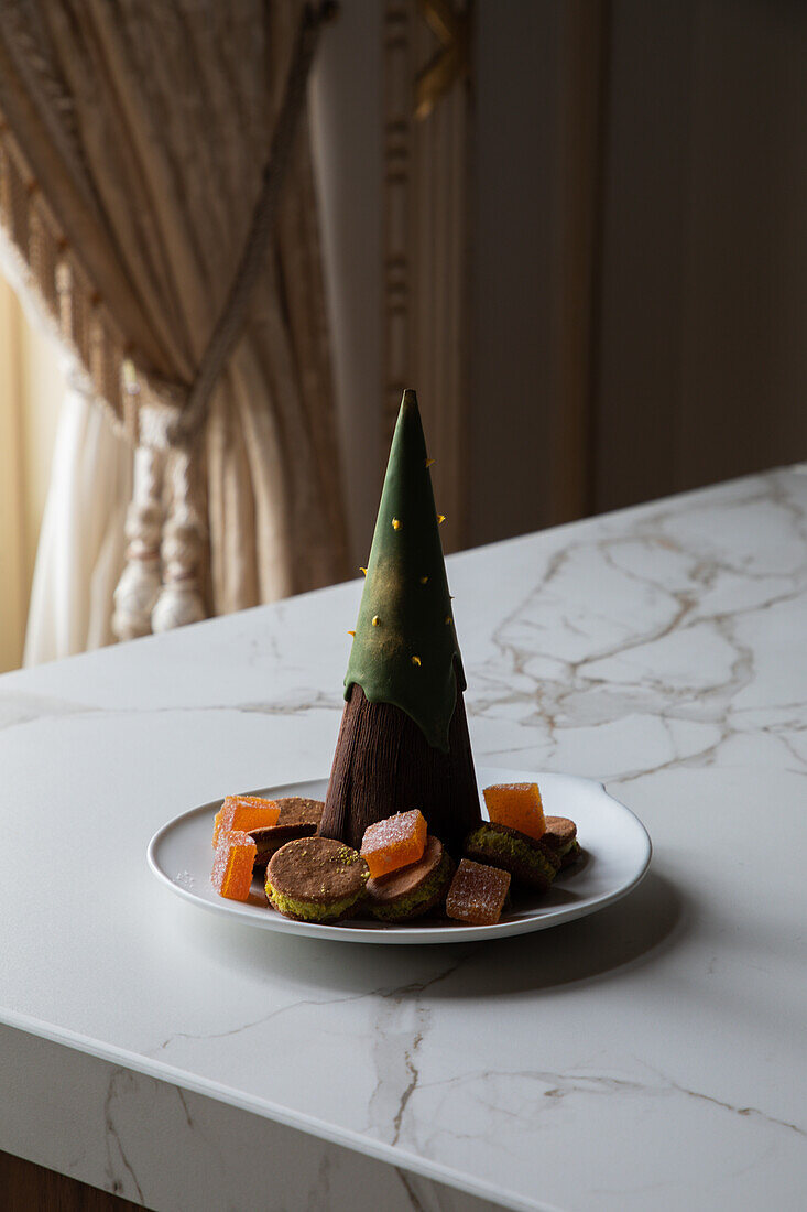 Schokoladendessert in Form eines Weihnachtsbaums auf einem Teller mit verschiedenen Keksen und Marmelade, serviert auf einem Marmortisch in einem stilvollen Restaurant