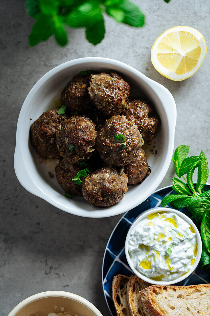 Top view of appetizing traditional homemade fried Greek meatballs served on gray background near plate with bread and lemon in kitchen